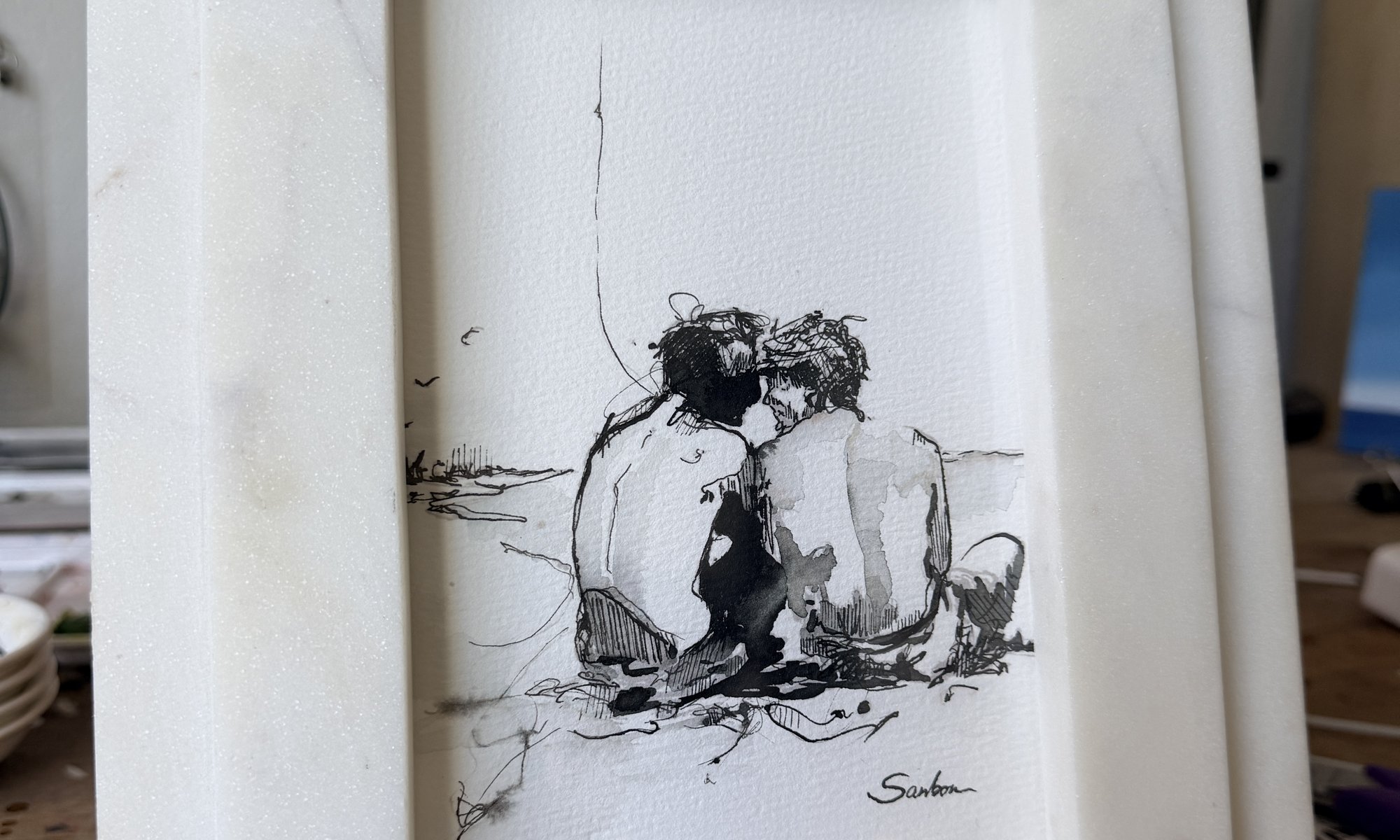 Brenden Sanborn's 5 by 7 ink drawing of two men on the beach in a white marble frame