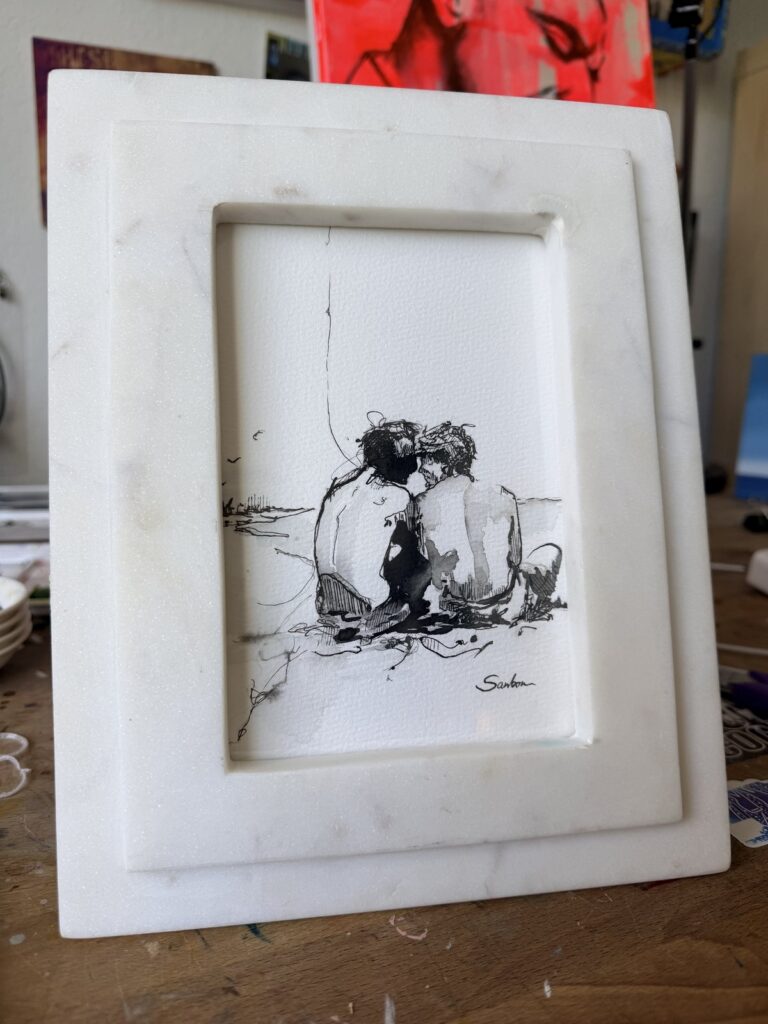 Brenden Sanborn's small ink drawing of two men sitting close on the beach, framed in white marble, in his studio