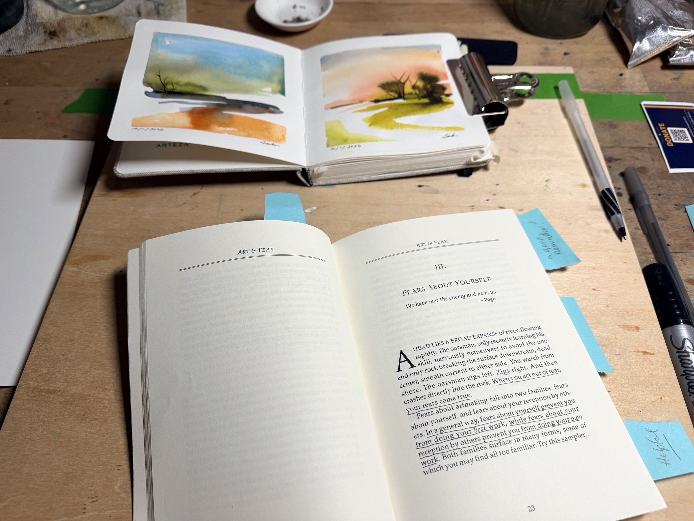 Art and Fear open on Brenden Sanborn's studio table, with his watercolor sketchbook and brushes behind it