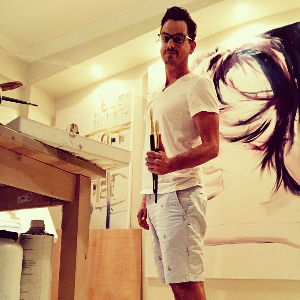Brenden Sanborn holding brushes in his Fort Lauderdale studio beside a large painting