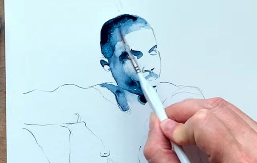 Brenden Sanborn painting an indigo watercolor portrait of a man, brush on the face, pencil sketch of the shoulders below