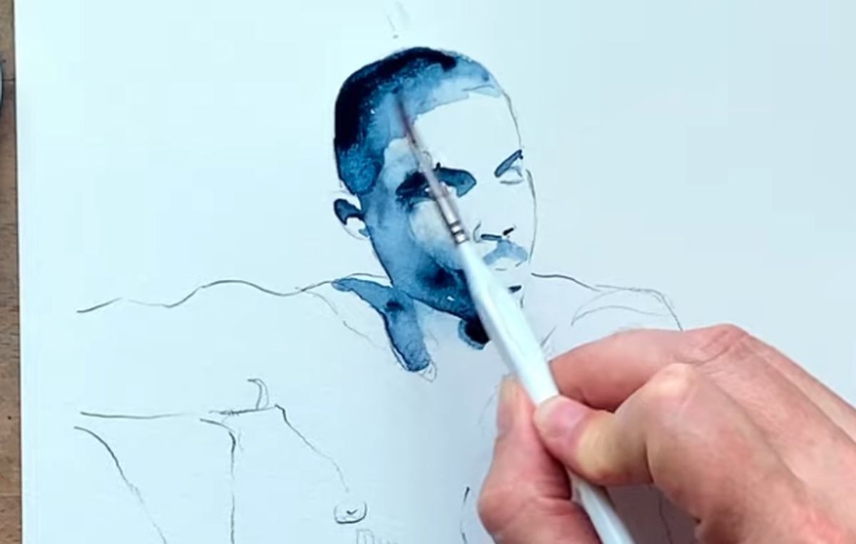 Brenden Sanborn painting an indigo watercolor portrait of a man, brush on the face, pencil sketch of the shoulders below