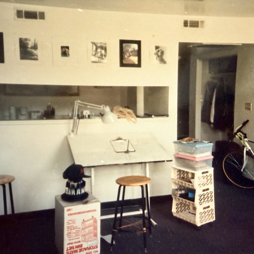 Brenden Sanborn's student studio in Savannah while at SCAD, with a drafting table, lamp, stool and photos pinned to the wall