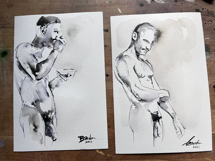 Two ink figure sketches by Brenden Sanborn on his paint spattered studio table